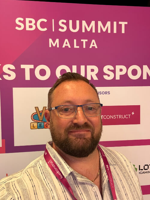 Chris Humphries of FTD Digital in front of a sign for the SBC Summit Malta conference 2025